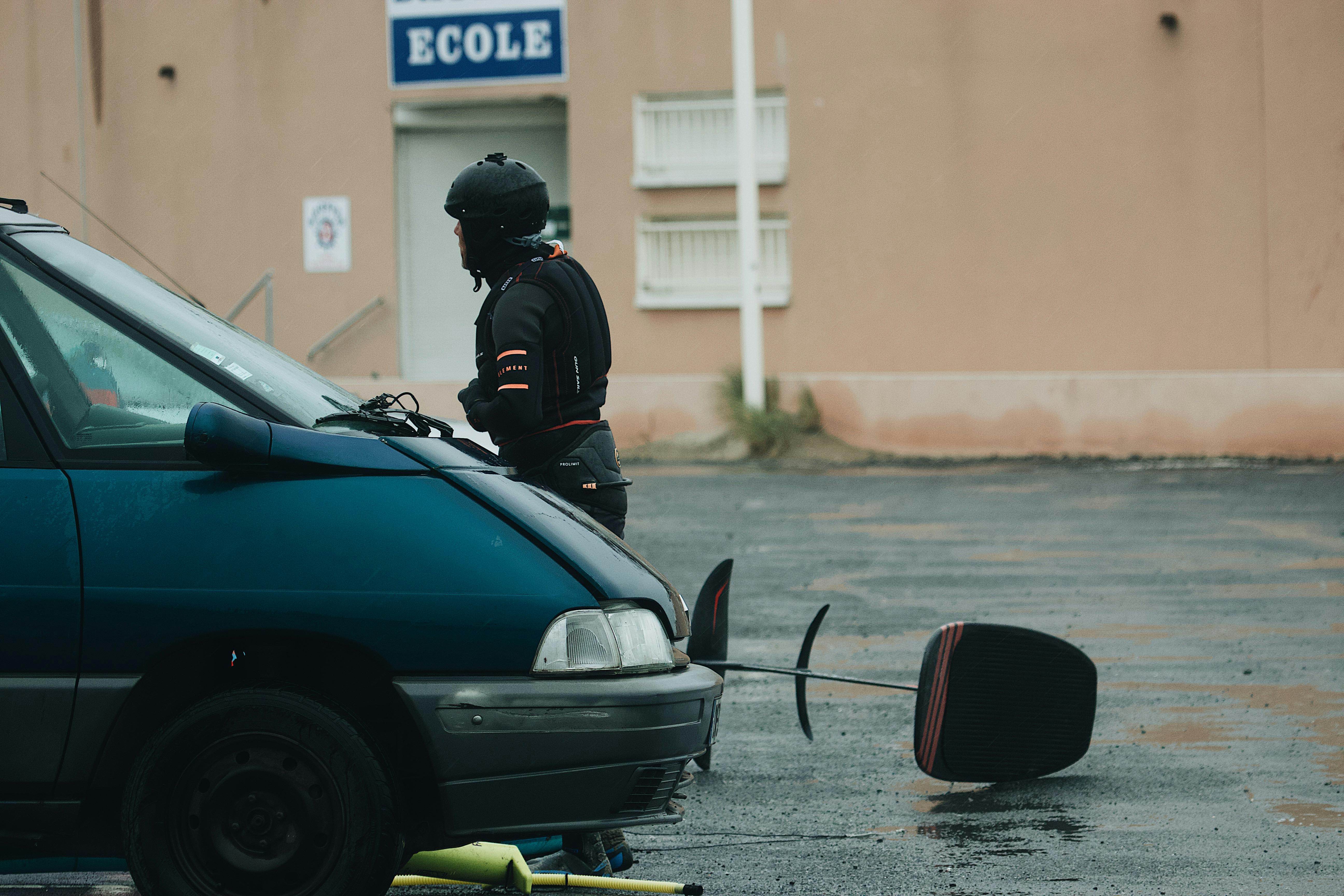 man in black helmet and black helmet standing beside blue car