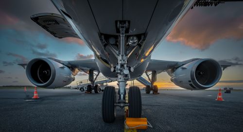 Free Close-up of an airplane's undercarriage with sunset sky, highlighting the landing gear and engines. Stock Photo