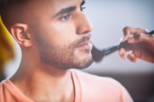 Close-up of a man having makeup applied with a brush by an artist.