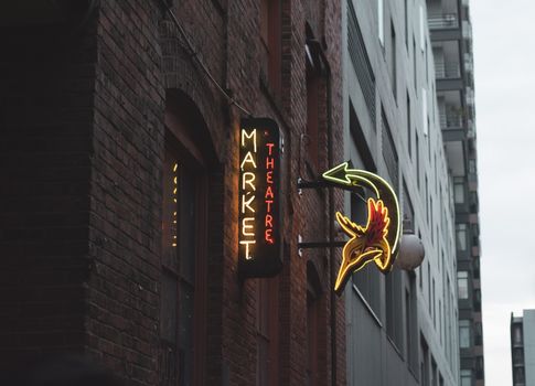 Neon sign for Market Theatre on a brick wall in a city alleyway, featuring vibrant colors.