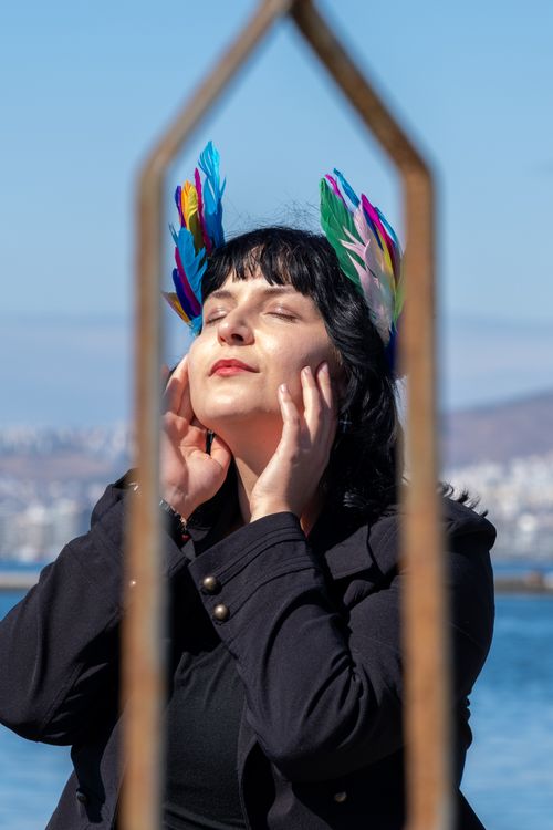 Free A woman with colorful feather headpiece enjoying sunlight by the waterfront. Stock Photo