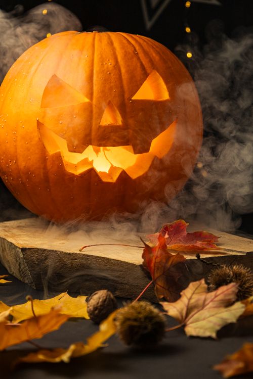 Free Carved pumpkin glowing with spooky fog and autumn leaves, perfect for Halloween themes. Stock Photo