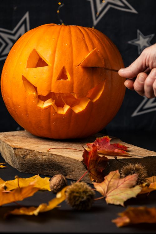 Free A hand carves a playful jack-o'-lantern amidst autumn leaves, evoking a festive Halloween atmosphere. Stock Photo