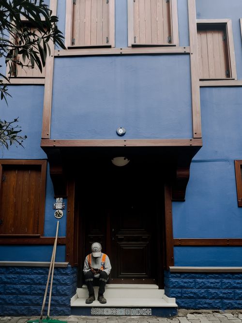 Free A worker in a reflective vest sits contemplatively by a vibrant blue building facade. Stock Photo