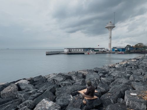 Free Person fishing by rocky shore near lighthouse under a cloudy sky. Stock Photo