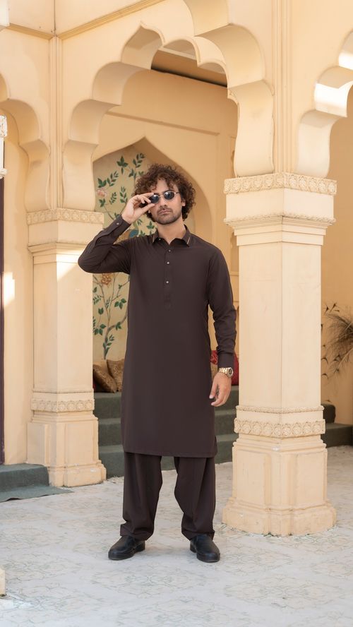 Free Man in brown kurta and sunglasses posing in ornate setting, showcasing traditional fashion. Stock Photo