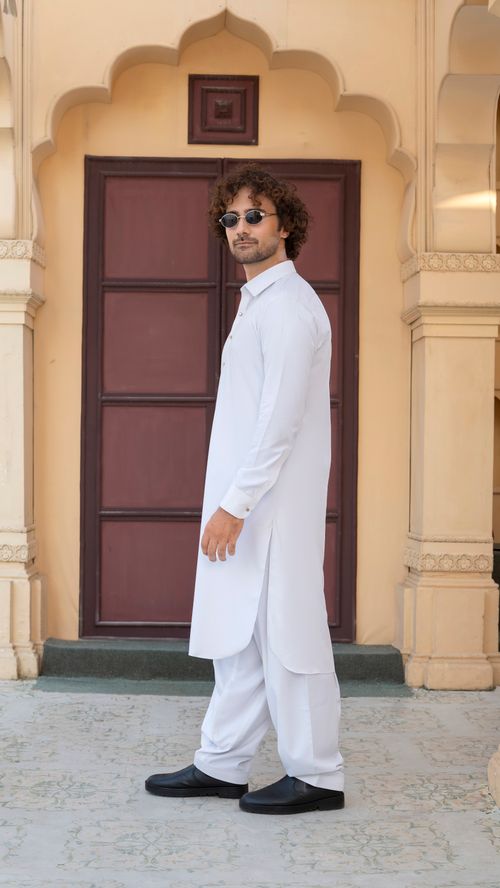 Free A fashionable man poses in traditional white attire with a historic architectural backdrop. Stock Photo