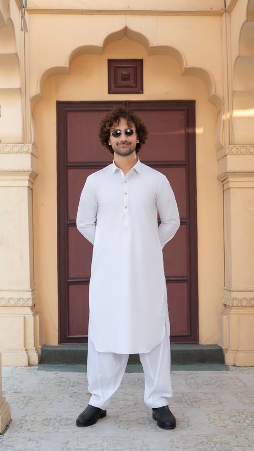 Free Adult male wearing a white kurta and sunglasses stands in front of an ornate door. Stock Photo