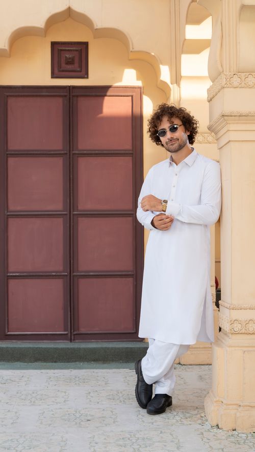 Free Man in traditional white attire stands confidently by an ornate doorway, exuding style and cultural elegance. Stock Photo