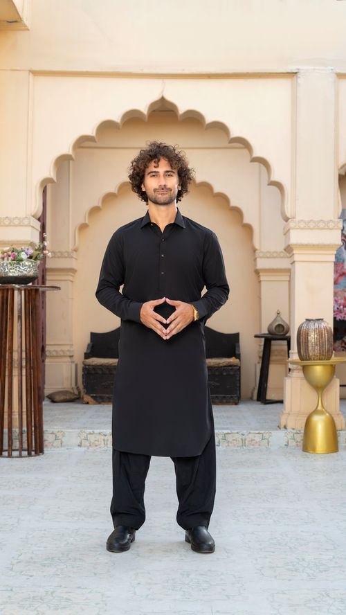 Free Portrait of a man in traditional black attire standing confidently in a courtyard. Stock Photo