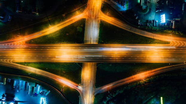 Drone shot of a brightly lit highway intersection glowing at night, showcasing vibrant urban infrastructure.