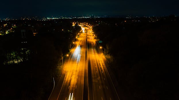 Aerial nighttime view of a brightly lit highway with glowing streetlights and moving car lights.