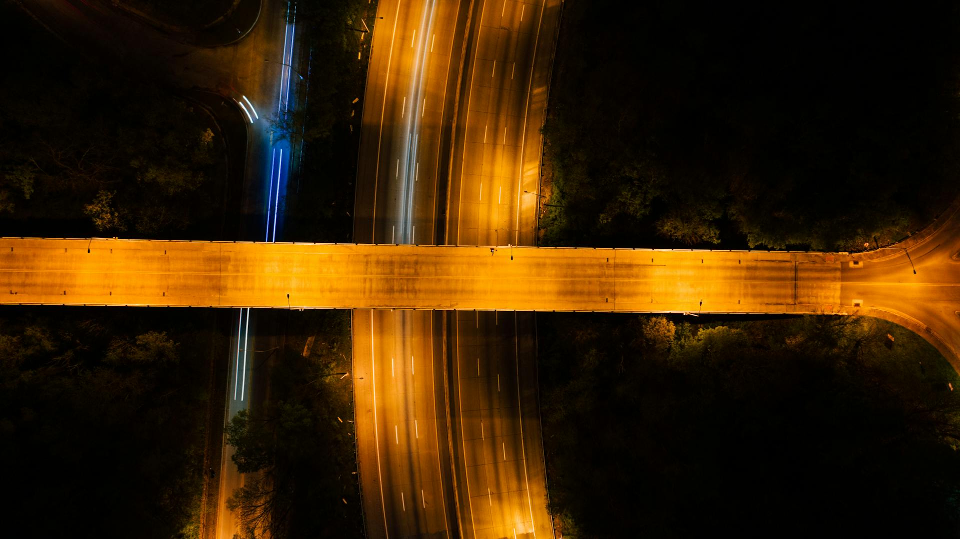 Drone aerial view capturing an illuminated highway intersection at night with flowing traffic lights.