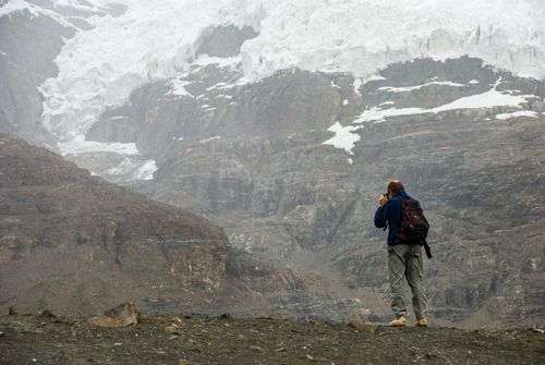 Free A lone photographer capturing the majestic glacier amidst rugged mountain terrain. Stock Photo