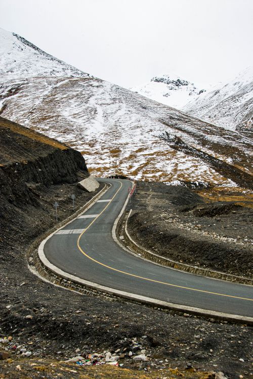Free A winding road through a mountainous landscape with snow-capped peaks, illustrating the beauty of winter wilderness. Stock Photo