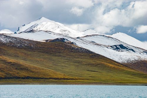 Free Snow-covered peaks with a calm lake in the foreground under cloudy skies. Stock Photo