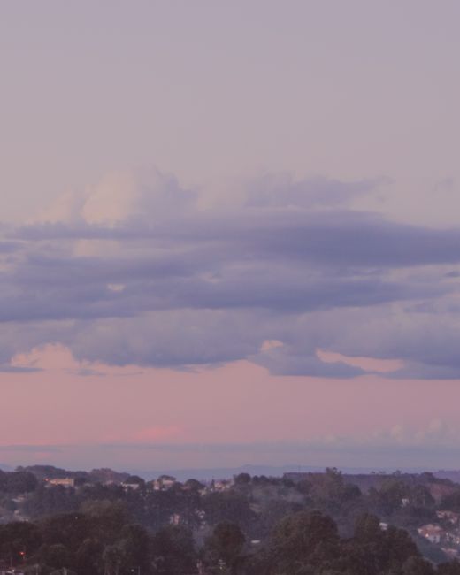 Scenic view of sky with pink clouds on sunset above endless ocean and settlement immersed in greenery