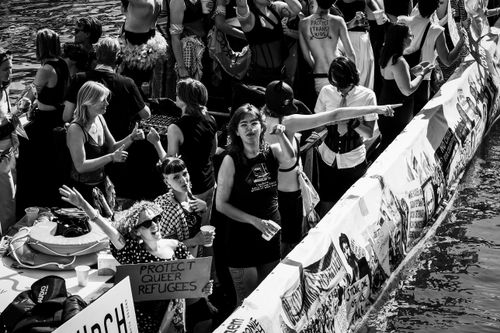 Free Black and white image of a lively LGBTQ+ pride parade on an Amsterdam canal with signs and diverse crowd. Stock Photo