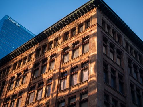 Free A historic brick building contrasted with a modern glass skyscraper in the background at sunset. Stock Photo