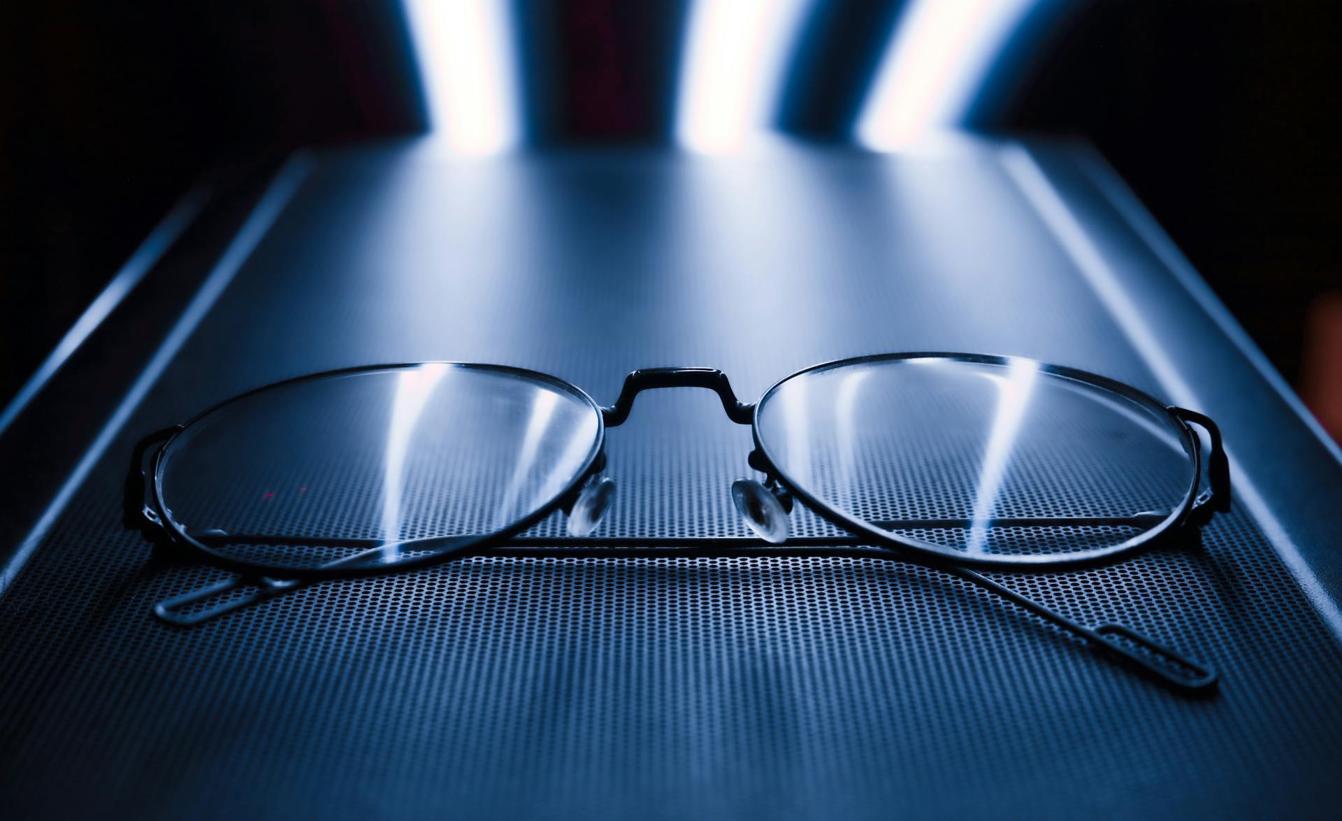 Close-up shot of eyeglasses with a dark blue background and reflective blue light.