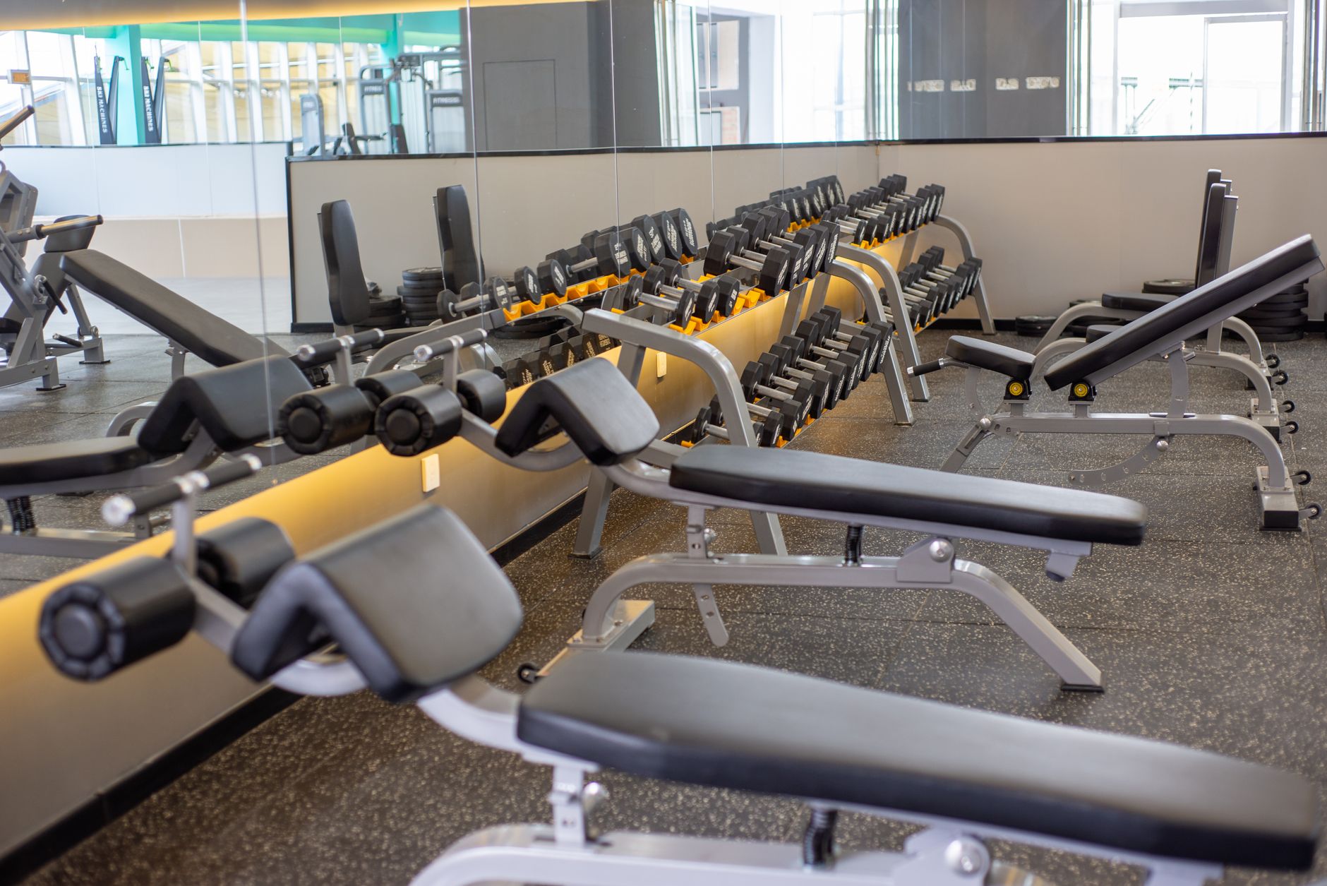 Empty gym with lined-up dumbbells and benches reflecting in a mirror, ready for workout.