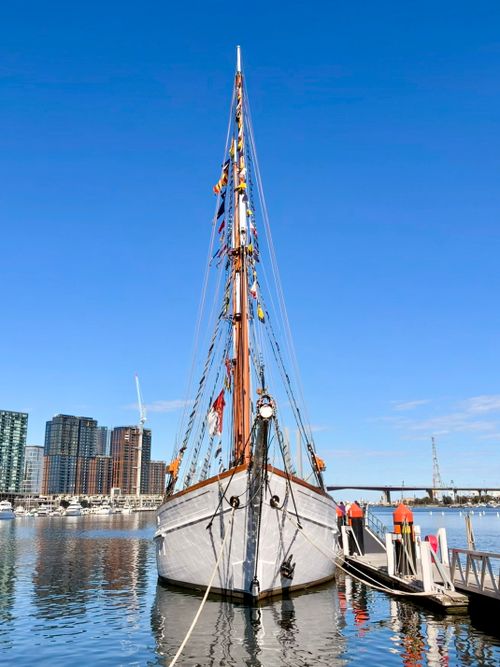 Free Majestic tall ship docked at serene Docklands with city skyline backdrop under clear blue skies. Stock Photo