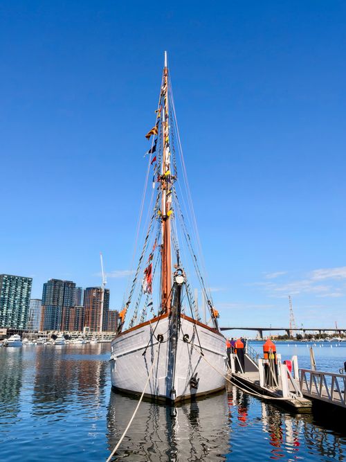 Free A classic sailing ship docked in Docklands, Victoria, with city skyscrapers in the background. Stock Photo
