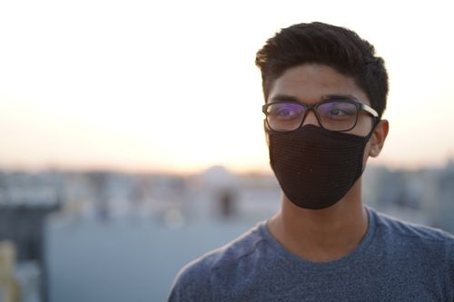 Free Portrait of a young man wearing eyeglasses and a mask outdoors at sunset, embracing the new normal. Stock Photo