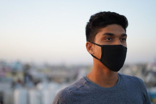 Free Portrait of a young man wearing a face mask, standing outdoors during the daytime. Stock Photo