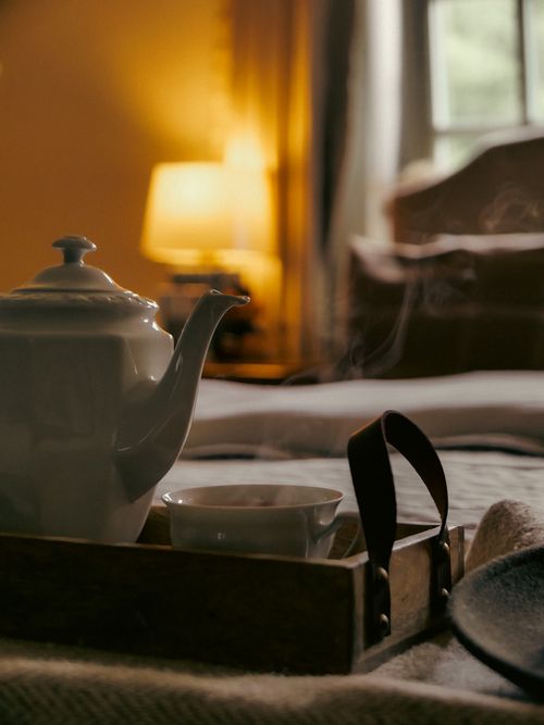 Free A steaming pot of tea on a tray in a cozy, warmly lit bedroom with elegant decor. Stock Photo