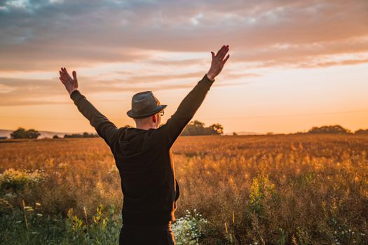 A person joyfully raises their arms in a sunny field at sunset, embracing nature.