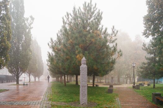 A foggy autumn morning in a Kyiv park with a prominent statue and misty atmosphere.