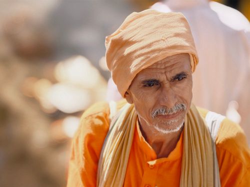Free Portrait of an elderly man wearing traditional orange clothing and headgear, photographed outdoors during the day. Stock Photo
