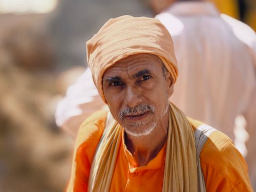 Free A close-up portrait of an older man wearing traditional orange attire and headscarf outdoors. Stock Photo