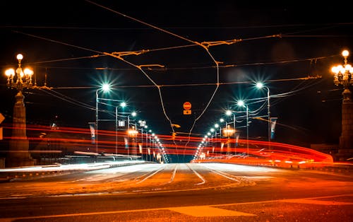 Picturesque long exposure of broad road with red light of fast traffic under street lamps on bridge at night
