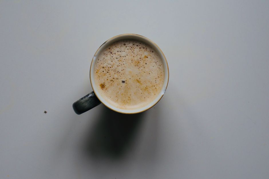 Top-down view of a cup filled with frothy coffee on a minimalist gray surface.
