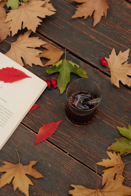 Free Cozy autumn setup with colorful leaves, an open book, and a drink on a wooden table. Stock Photo