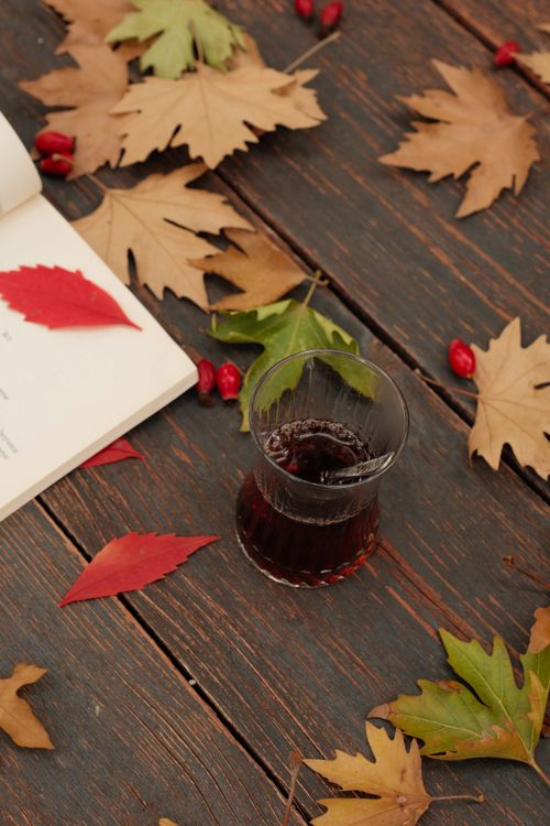 Free Cozy autumn scene with a warm drink, fallen leaves, and an open book on a wooden table. Stock Photo