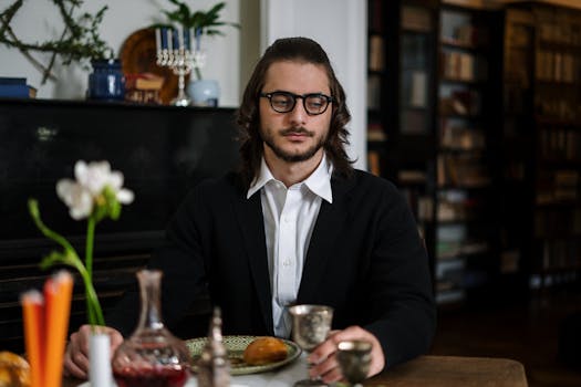 Adult man in glasses sits at a table during Hanukkah, surrounded by traditional decorations.