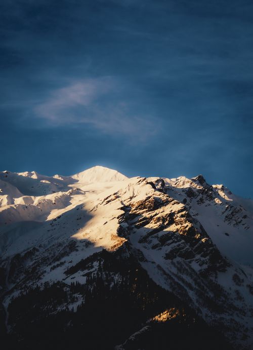 Free Beautiful snow-capped mountain peak illuminated by the warm glow of sunset, under a clear blue sky. Stock Photo