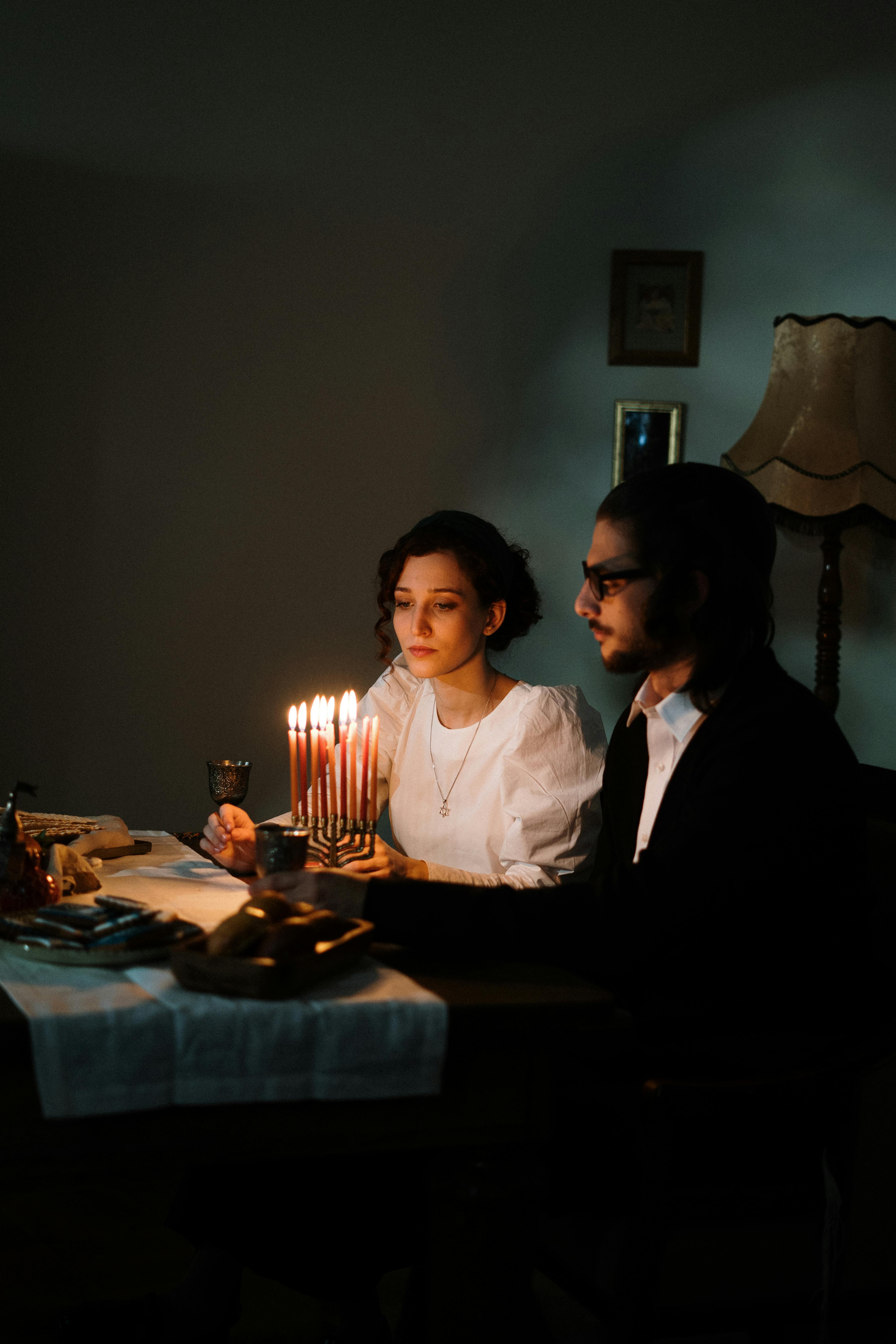 A couple celebrates Hanukkah at home by candlelight, embracing tradition and warmth.