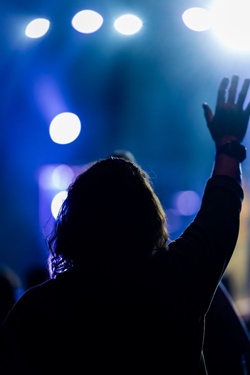Free Silhouette of an adult at a lively concert, hand raised amidst stage lights. Stock Photo