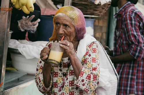 Free Elderly woman sipping juice at a vibrant outdoor market, embracing local flavors. Stock Photo