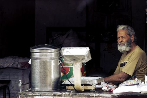 Free Senior man at a traditional market stall with weighing scale, conveying rural life. Stock Photo