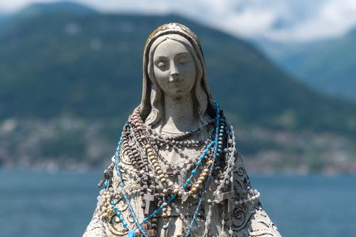 Free A peaceful statue of Mary, draped with colorful rosary beads, set against a mountainous backdrop. Stock Photo