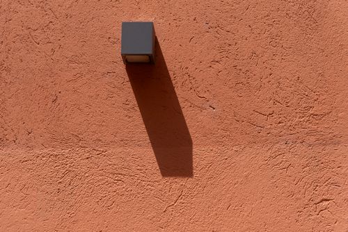 Free Artistic shadow on textured terracotta wall from geometric light fixture. Stock Photo