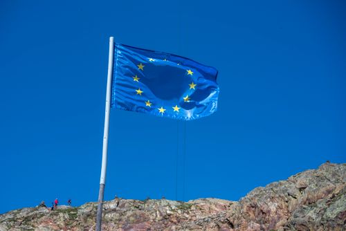 Free European Union flag waving atop a rocky hill with clear blue sky backdrop. Stock Photo