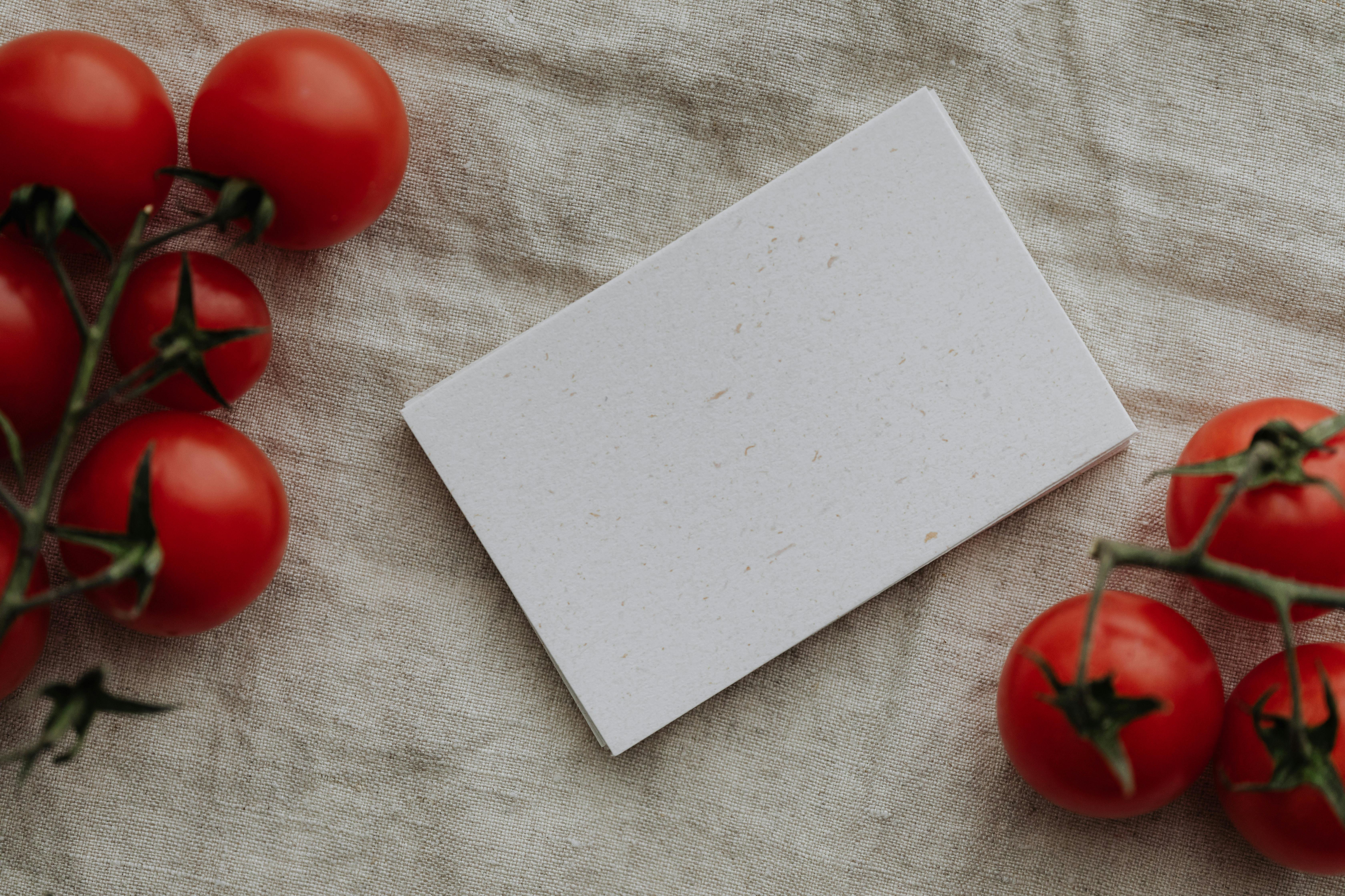 Rustic flat lay featuring fresh cherry tomatoes and a blank card on linen fabric. Perfect for creative mockups.