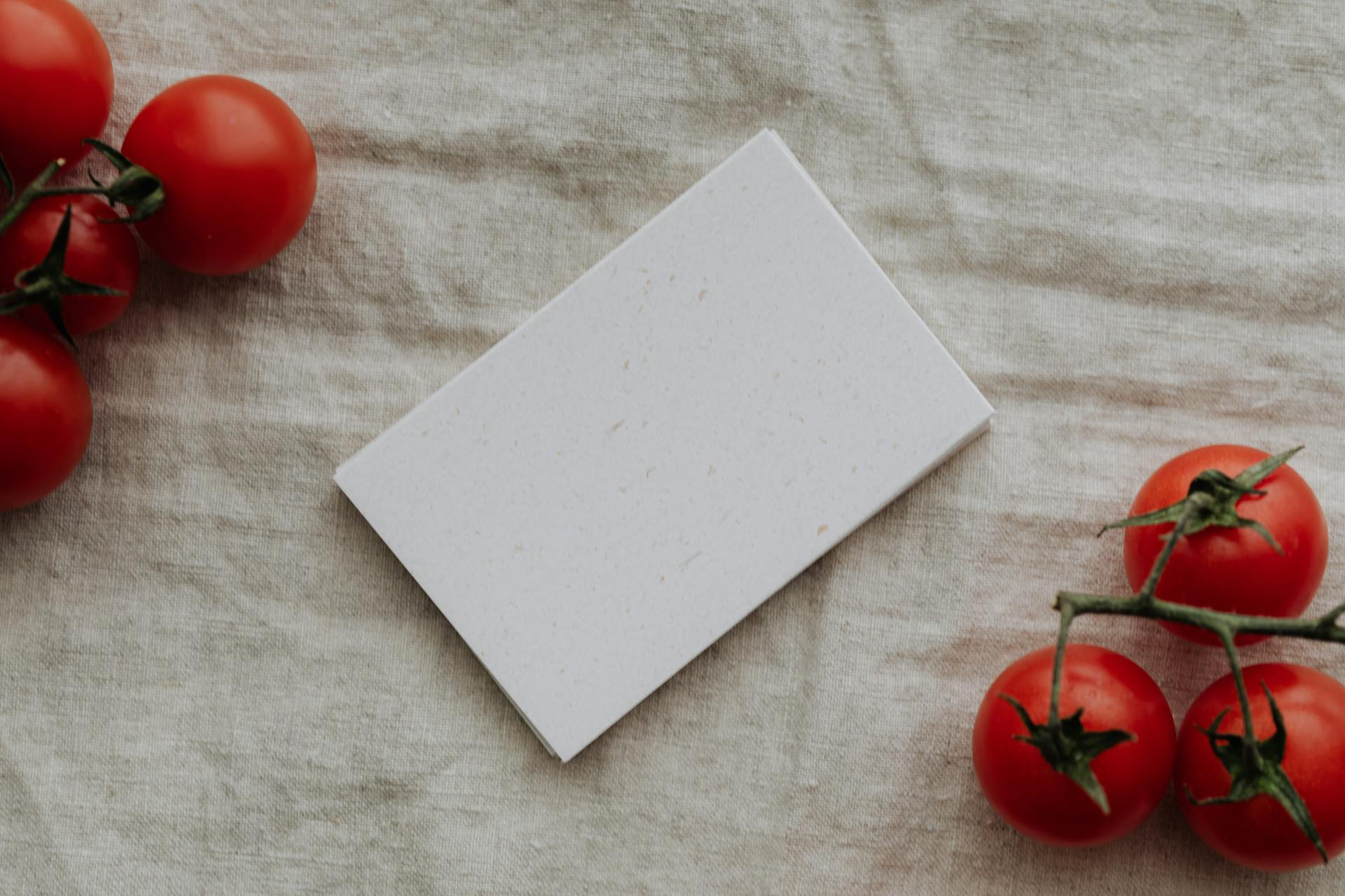 Minimalist flat lay with blank card on linen cloth surrounded by cherry tomatoes, ideal for mockups.