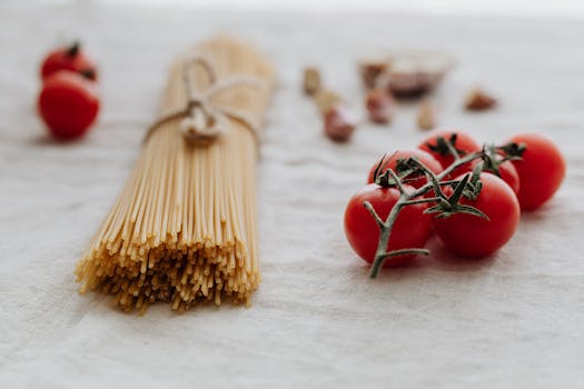 Aesthetic flat lay of dry spaghetti and fresh tomatoes on a linen backdrop.